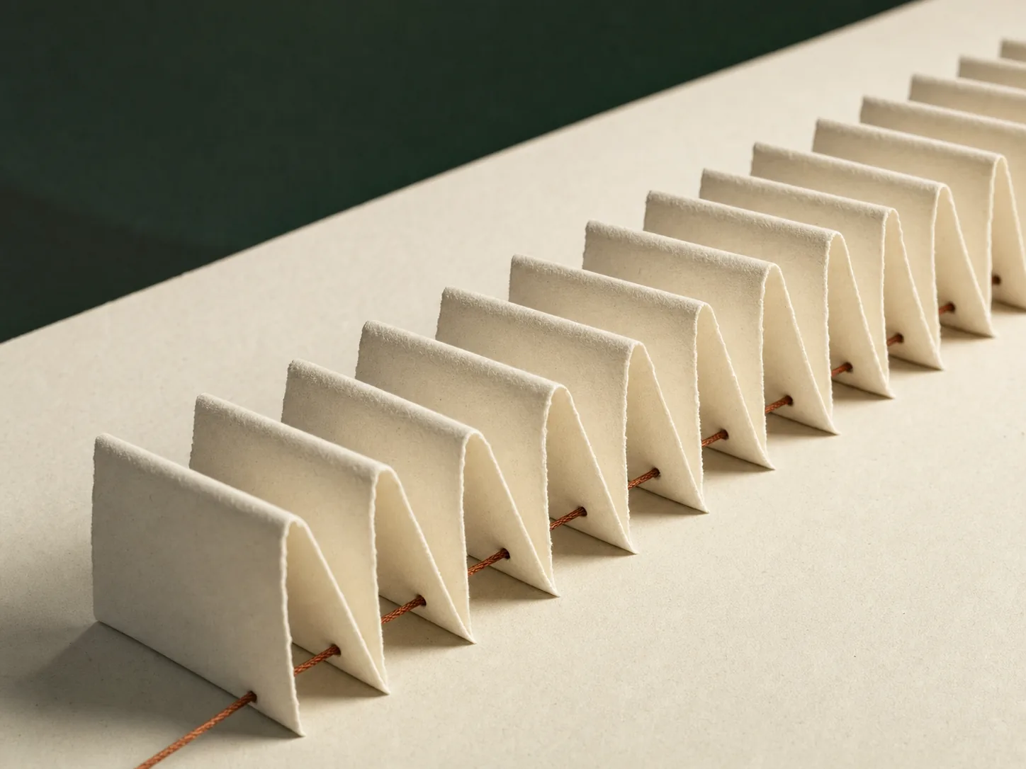 A receding row of identical cream paper pleats with a single copper thread running through them